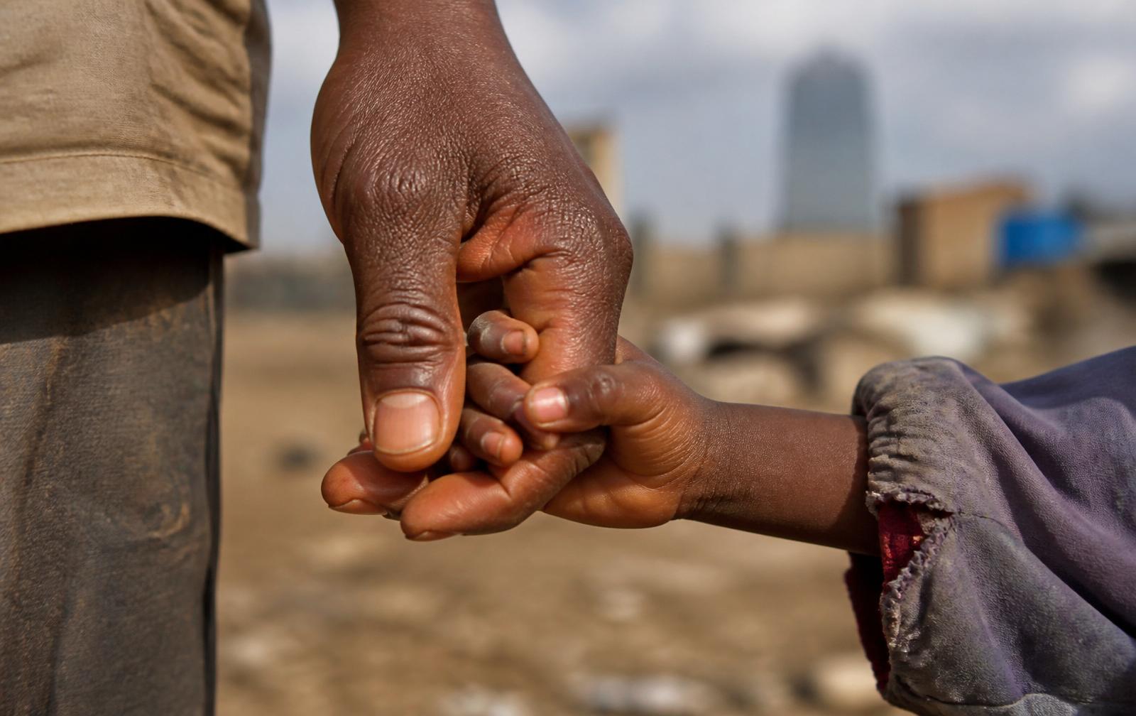 An African man's hand gently holding a child's hand — clinical outreach with street-connected children in Nairobi